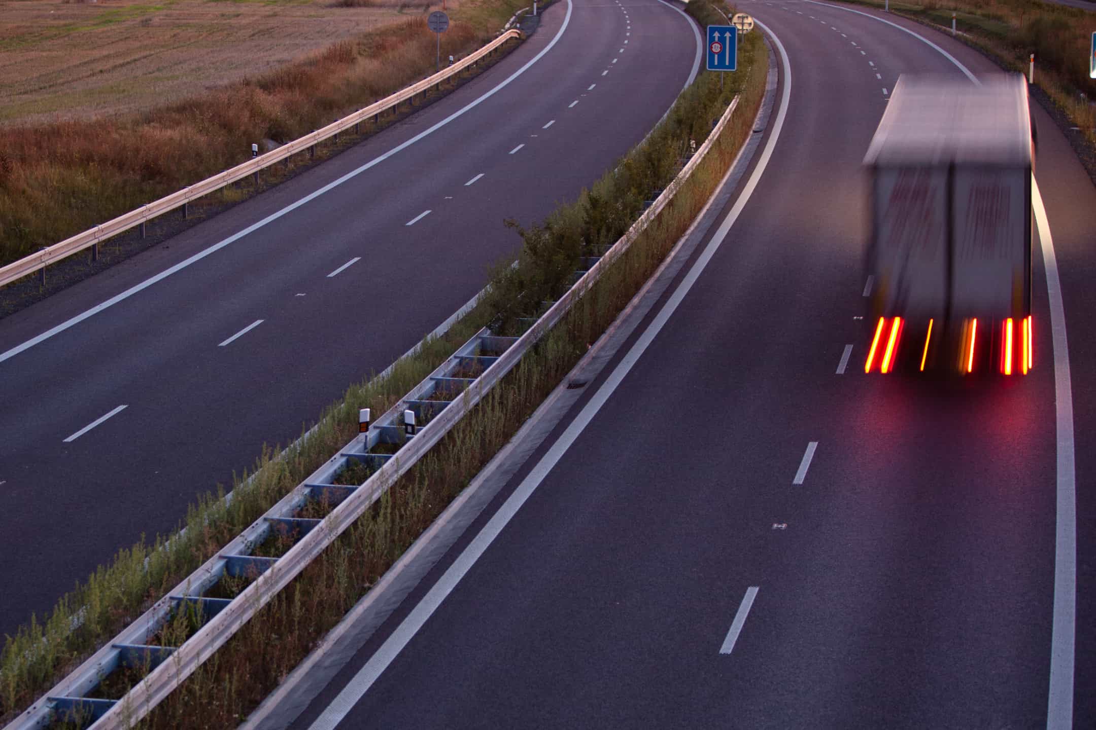 A blurry delivery truck driving along a highway at dusk